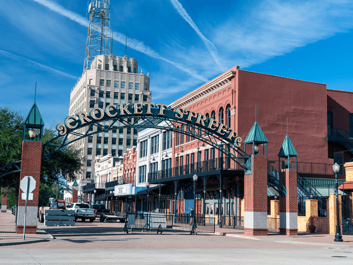 An iron archway reading Crockett Street marks the entrance to a historic downtown district lined with red brick and white buildings under a clear blue sky.