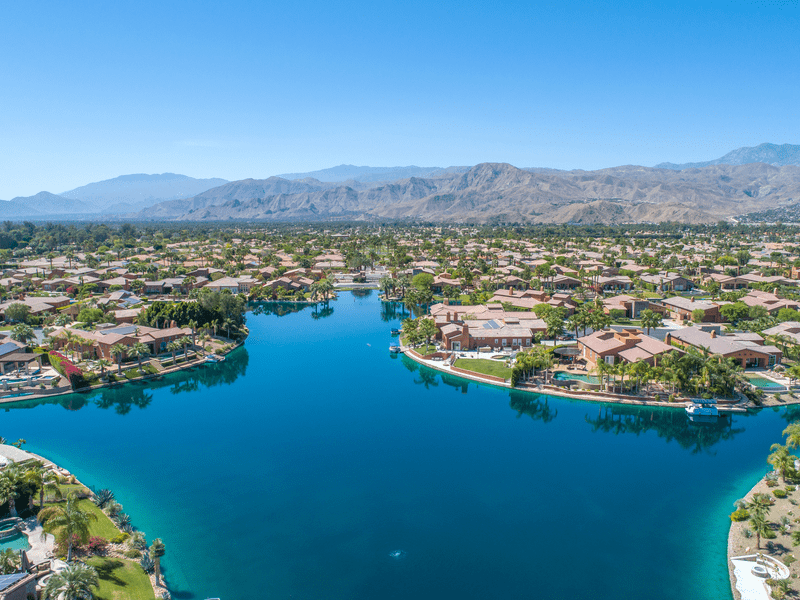 Aerial view of a residential neighborhood surrounding a large, clear blue lake, with mountains in the background under a clear sky.